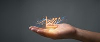 Glowing upward trending arrow chart with sparkles floating above open palm against gray background for business growth concepts.