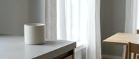 Minimalist workspace with empty white mug on gray desk, natural light from window, modern interior design for home office or creative workspace.