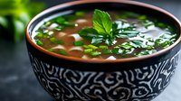 Fresh herb soup with green vegetables and basil garnish served in decorative ceramic bowl on dark surface for healthy dining and culinary content.