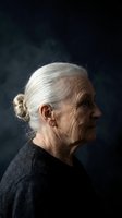 Senior woman with white hair in bun, wearing dark sweater, profile view against dark background. Suitable for aging, healthcare, and lifestyle editorial use.