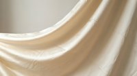 Soft beige fabric with elegant flowing folds and gentle curves creating luxurious textile waves in warm neutral tones for interior design and fashion.