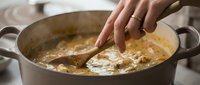 Woman stirring creamy soup in large pot with wooden spoon. Home cooking, comfort food preparation in kitchen. Culinary skills and meal preparation concept.