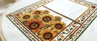 Cross stitch embroidery hoop with sunflower pattern on white fabric. Handmade needlework craft project with colorful floral design for home decor and textile art.
