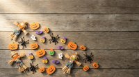 Halloween decorations with orange pumpkins, black spiders and purple bats scattered on rustic wooden background for seasonal party planning and festive designs.