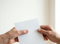 Mature adult hands holding blank white card or paper against neutral background, suitable for business messaging, greeting cards, invitations, and promotional materials.