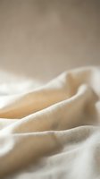 Soft beige linen fabric with natural folds and wrinkles creating organic texture for interior design and textile backgrounds.