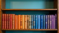 Colorful vintage books arranged on wooden bookshelf creating rainbow gradient from red to purple spines for library and education concepts.