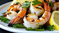 Grilled jumbo shrimp and prawns garnished with fresh parsley and lemon slices on white plate, close up view of succulent seafood appetizer with char marks.