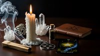 Mystical fortune telling setup with burning candle, tarot cards, crystal ball, incense smoke and ancient books on dark wooden table for divination.