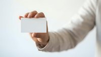 Person in beige business attire holding blank white card, suitable for corporate branding, business cards, contact information, and professional marketing materials.