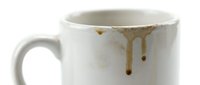 Ceramic mug with coffee stains and drips on white surface, suitable for beverage, lifestyle, and product photography projects.