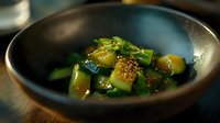 Fresh cucumber salad with sesame seeds in dark ceramic bowl, garnished with green onions and Asian-inspired dressing. Healthy vegetarian appetizer.