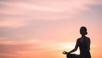 Woman practicing yoga meditation at sunset with peaceful pink sky creating serene wellness atmosphere for mindfulness and spiritual balance.