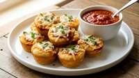Golden baked egg muffins with cheese and herbs served on white plate with marinara dipping sauce, perfect for breakfast or brunch meal preparation.