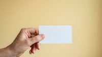 Male hand holding blank white business card against neutral beige background, suitable for branding, corporate identity, and marketing mockup presentations.