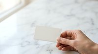 Caucasian hand holding blank white business card against marble surface for corporate branding and professional networking purposes.