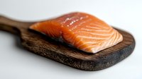 Fresh raw salmon fillet with visible texture and marbling on rustic wooden cutting board against white background, selective focus for food photography.