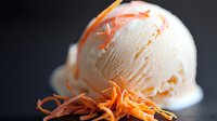 Creamy vanilla ice cream scoop garnished with fresh orange zest curls on dark background, selective focus creates appetizing dessert presentation.