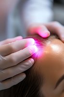 Red light therapy treatment on forehead area during cosmetic procedure, close up view of therapist hands in protective gloves performing LED skincare session.
