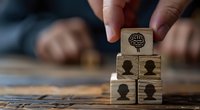 Wooden blocks with human head silhouettes and brain symbol arranged in pyramid shape, representing team leadership, mental health, or organizational psychology concept for business design.