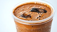 Iced coffee with chocolate pieces in plastic cup with condensation drops on surface. Close up view of cold brew coffee drink with foam bubbles.