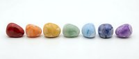 Polished gemstones in rainbow colors arranged in a row on white background, representing chakra healing crystals for wellness, meditation, and alternative therapy practices.