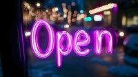 Glowing purple neon open sign in window with blurred city lights and bokeh background creates welcoming nighttime business atmosphere.
