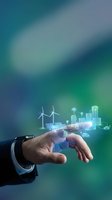 Businessman hand holding holographic smart city with wind turbines and solar panels representing renewable energy and sustainable urban development technology.