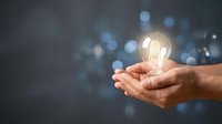 Hands holding glowing light bulb with bokeh background representing innovation, creativity, inspiration and bright ideas for business solutions.