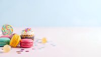 Colorful macarons, cupcake and lollipop arranged on pastel pink surface with copy space for sweet dessert and bakery marketing materials.