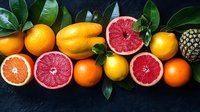 Fresh citrus fruits arrangement with grapefruit, oranges, lemons and pineapple on dark background with green leaves, top view food photography.