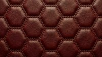 Luxurious brown leather upholstery with hexagonal quilted pattern and decorative stitching for premium furniture and automotive interior design projects.