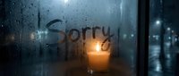 The word Sorry written on a foggy rainy window with a glowing candle, evoking emotions of regret, apology, and melancholy on a dark night.