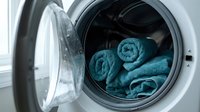 Blue towels rolled and placed inside modern washing machine drum with open door for laundry and household cleaning tasks.