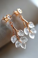 Delicate rose gold earrings with translucent crystal leaves and flower studs on soft gray background. Elegant jewelry macro photography for fashion accessories.