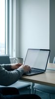 Professional working on laptop at modern office desk with coffee cup near window for remote work and business productivity.