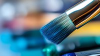 Professional makeup brush with blue synthetic bristles and metallic handle against blurred colorful background, macro photography showing fine details and texture.