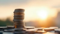 Stack of silver and copper coins on wooden surface against blurred sunset background, symbolizing financial growth, savings and investment planning.