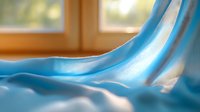 Soft blue silk fabric flowing gracefully with warm sunlight streaming through window creating elegant waves and gentle shadows for luxury textile design.