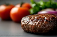 Grilled beef burger patty with fresh tomatoes and red onion on dark surface for cooking and food preparation concepts.