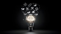 Glowing light bulb with business icons floating above on dark background representing innovation, creativity and entrepreneurial ideas for startup success.
