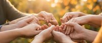 Diverse group of people joining hands together in circle outdoors during golden hour, symbolizing unity, teamwork, community support and togetherness for corporate or nonprofit campaigns.