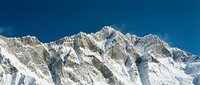 Majestic snow-covered mountain peaks rise against a clear blue sky, showcasing dramatic alpine terrain with steep rocky slopes and pristine white snow coverage ideal for travel and nature content.