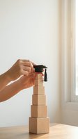 Hand placing graduation cap on wooden blocks tower representing educational achievement and career growth steps in bright modern interior.