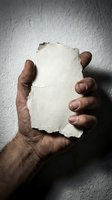 Male hands holding blank torn paper piece against textured wall background for message display and creative design projects.