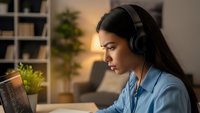 Young Hispanic woman wearing headphones working on laptop in modern home office during golden hour lighting for remote work and productivity.