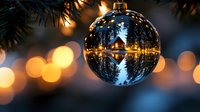 Blue Christmas ornament with winter village scene reflection hanging on evergreen tree with warm golden bokeh lights creating festive holiday atmosphere.