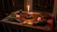 Mystical altar setup with burning candle, crystals, herbs and ritual tools on ornate cloth for spiritual practices and meditation ceremonies.
