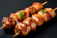 Grilled chicken yakitori skewers with glazed teriyaki sauce and fresh herbs garnish on dark background, close up view of traditional Japanese cuisine.