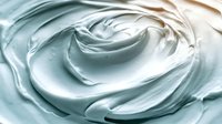 Smooth swirling texture of white cream or moisturizer with soft blue tint creates luxurious cosmetic background pattern. Close up macro photography shows silky surface.